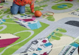 Chłopiec toczy dynie po torze na dywanie.