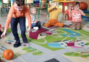 Chłopiec toczy dynie po torze na dywanie.