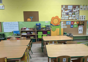 sala grupy Pszczółki, na pierwszym planie trzy stoliki z krzesłami w tle półki z zabawkami, tablice ze zdjęciami