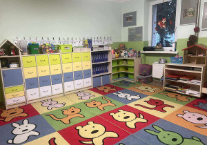 na pierwszym planie kolorowy dywan w zwierzątka, na drugim półki z zabawkami oraz materiałami plastycznymi