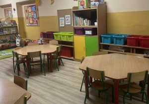 na pierwszym planie trzy stoliki z krzesłami, na drugim półki z zabawkami