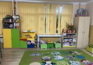 kolorowy dywan z wizerunkiem zwierząt, na drugim planie kolorowe półki z zabawkami